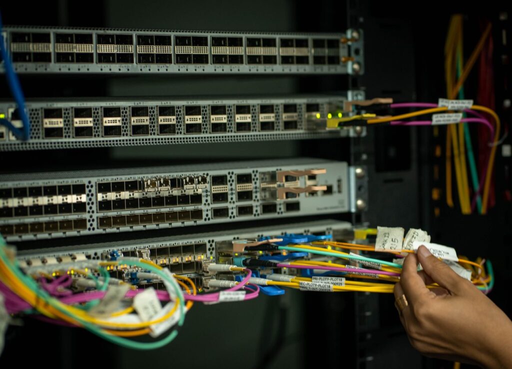 A hand managing fiber optic cables in a server room, showcasing modern connectivity.